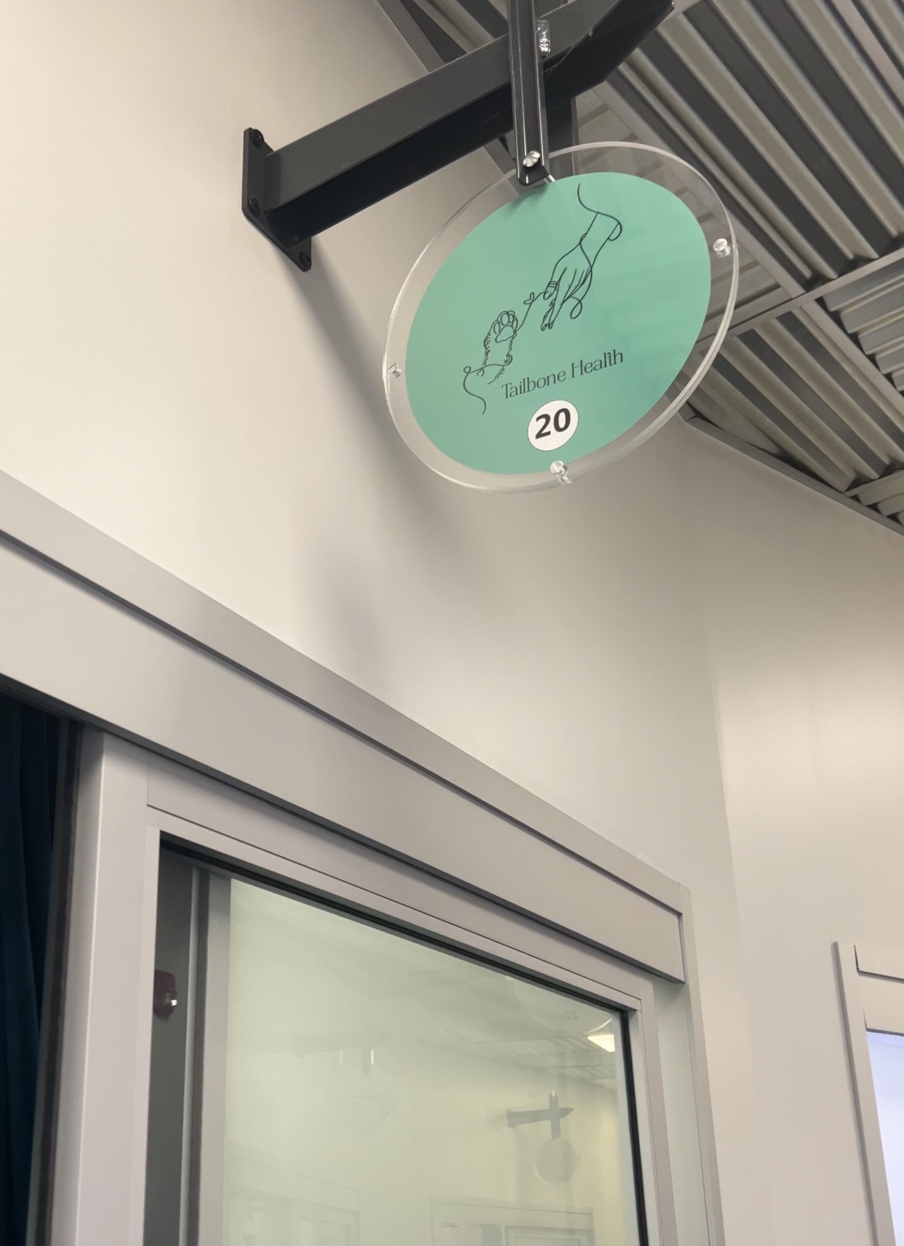The round mint Tailbone Health sign above the clinic door, room 20